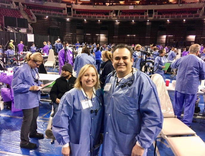 Trina Poulsen and Santiago Valdez in blue dentistry clothing at a dentistry event conference with people in the background.